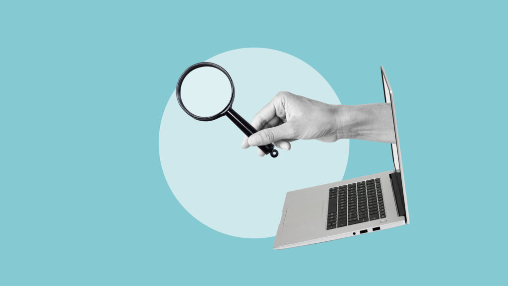 A hand holding a magnifying glass emerges from an open laptop screen against a blue background with a large white circle.