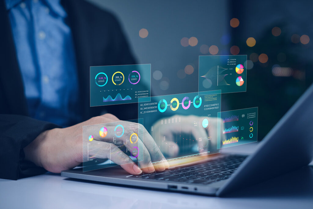 A person using a laptop with colorful, transparent data charts and graphs projected above the keyboard, suggesting data analysis or business analytics in a modern, high-tech environment.
