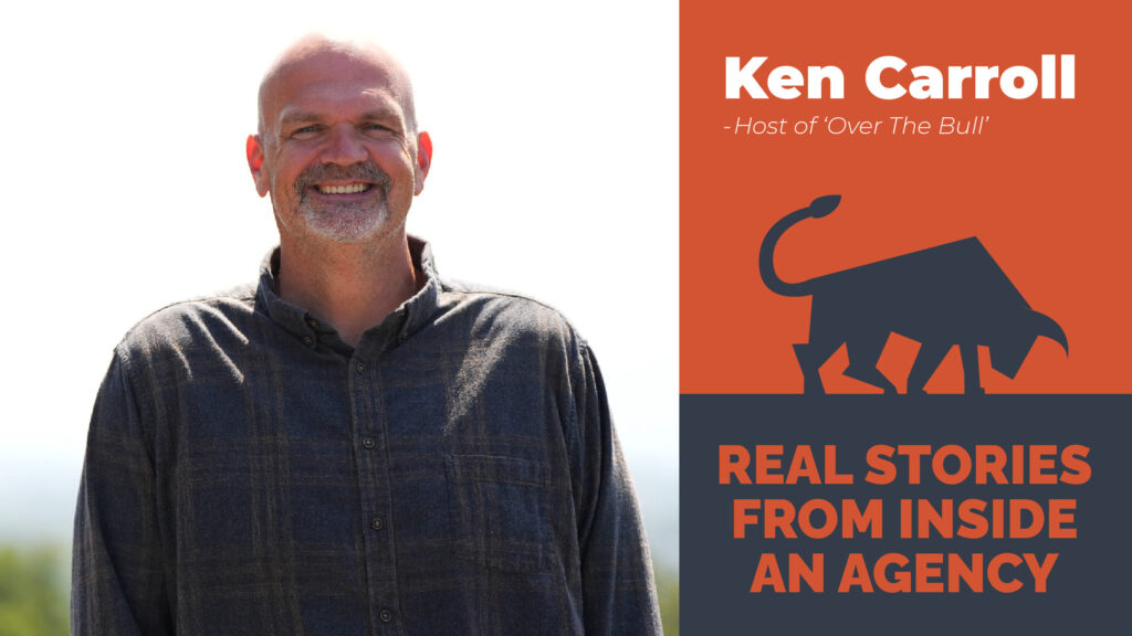 A smiling man in a dark shirt stands outdoors under a clear blue sky. A graphic next to him reads: Ken Carroll - Host of Over The Bull with a stylized bull icon. Text below says, Real Stories From Inside An Agency, offering insights from a marketing podcast in Asheville, North Carolina.