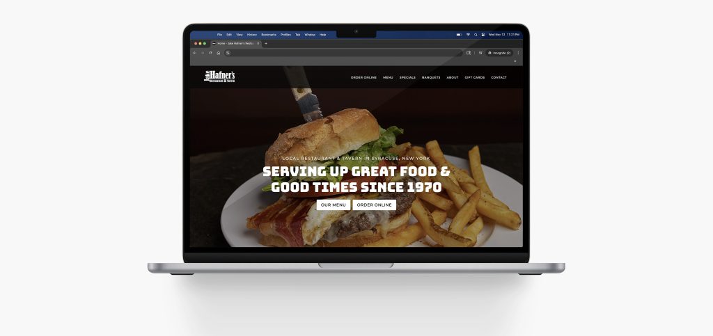 A laptop displaying a restaurant website with a background image of a sandwich, bacon, and fries. The screen reads: Serving up great food & good times since 1970 with buttons for the menu and online orders.
