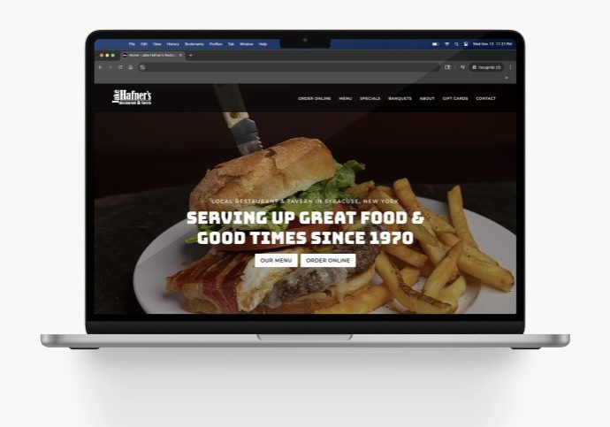 A laptop displaying a restaurant website with a background image of a sandwich, bacon, and fries. The screen reads: Serving up great food & good times since 1970 with buttons for the menu and online orders.